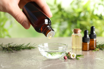 Woman dripping natural tea tree oil in bowl against blurred background, closeup