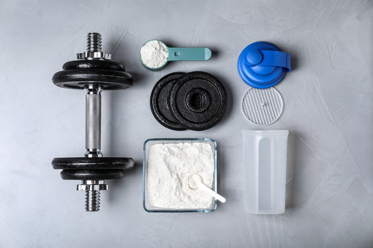 Flat lay composition with protein powder and dumbbell on grey background