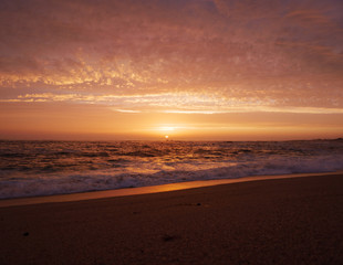 Fototapeta na wymiar Beautiful vivid sky at sunset on the beach as waves break on shore