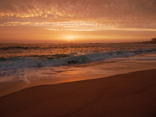 Fototapeta na wymiar Big waves break on beach at sunset in Portugal with beautiful sky