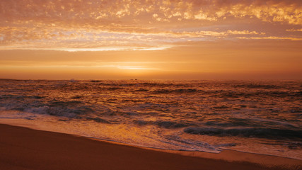 Fototapeta na wymiar Beautiful orange sky with clouds over ocean at sunset on the beach