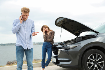 Young man and woman near broken car outdoors