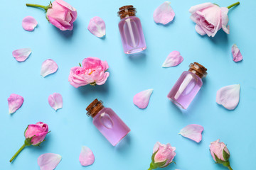 Fresh flowers, petals and bottles of rose essential oil on color background, flat lay