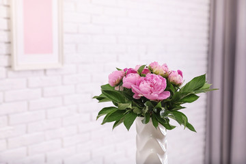 Vase with bouquet of beautiful peonies at white wall in room, space for text