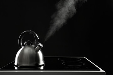 Modern kettle with whistle on stove against black background, space for text