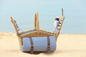 Fototapeta premium Wicker basket with picnic essentials on sand near sea