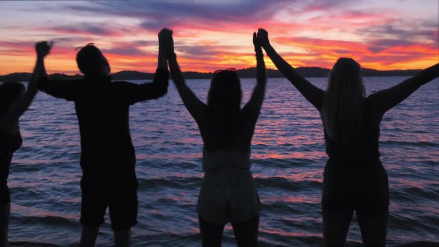 Tracking shot of a people celebrating and lifting their hands, at a beach, at lake Huma, on a sunny evening sunset, at Hume Reservoir, at New South Wales and Victoria, in Australia