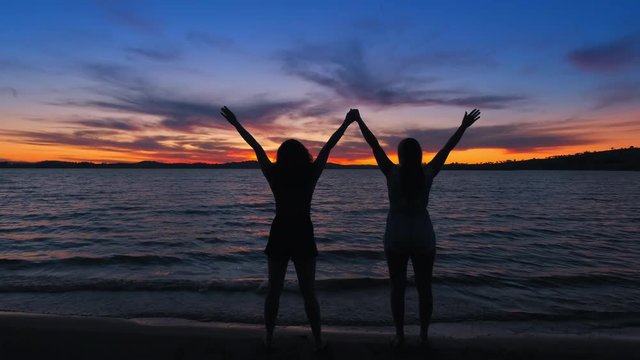 Dolly shot revealing people celebrating and lifting their hands, towards the sunset, at a beach, on a sunny evening dusk, at lake Huma, at Hume Reservoir, New South Wales or Victoria, in Australia