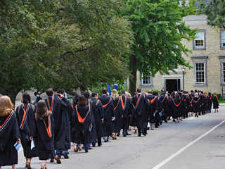 Procession of univesrsity students walking outdoors toward their graduation ceremony