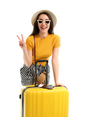 Happy young woman with suitcase showing victory gesture on white background