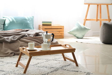 Small table with coffee pot and cups in stylish bedroom