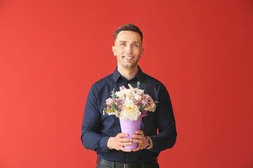 Handsome man with bouquet of beautiful flowers on color background