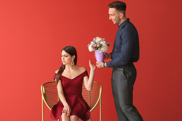 Offended young woman refusing to take bouquet of beautiful flowers from her boyfriend on color...