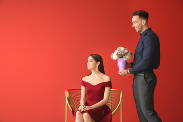 Offended young woman refusing to take bouquet of beautiful flowers from her boyfriend on color...