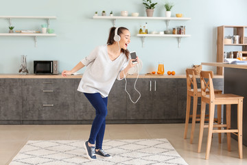 Beautiful woman listening to music in kitchen at home