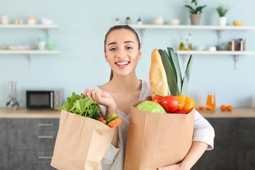 Beautiful woman with shopping bags full of fresh products in kitchen at home