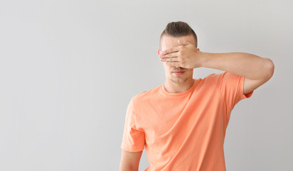 Young man covering his eyes on grey background