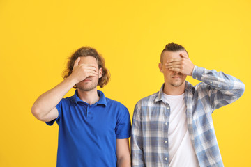 Young men covering their eyes on color background