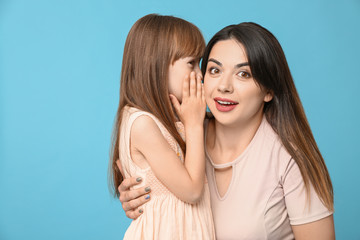 Little girl telling mother her secret against color background