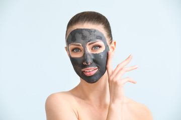 Beautiful young woman with facial mask on color background