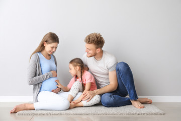 Beautiful pregnant woman with her family sitting near light wall
