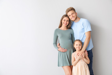 Beautiful pregnant woman with her family on light background