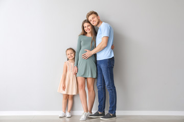 Beautiful pregnant woman with her family near light wall