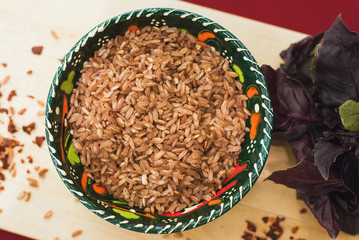 Zira rice lies in an oriental plate. dark rice lies on an oriental background, a golden tablecloth, a wooden cutting board next to basil.