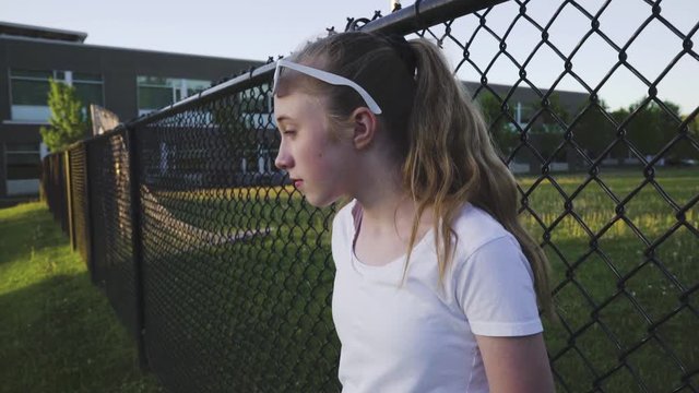 Sad girl leaning against a fence that is next to a school.