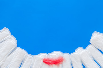 Menstruation calendar concept with sanitary pads and feather on blue background top view space for...
