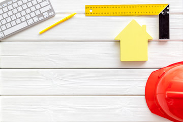 Constructor office desk with tools, helmet, ruler, keyboard and house figure on white wooden background top view mock up