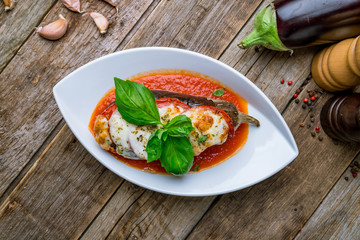 Parmigiano eggplant with basyl on white plate on wooden background