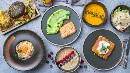 Foodset on table. poached egg with salmon and avocado on a white plate, burger, grilled salmon with mashed beens, pumpkin soup, carbonara and oatmeal porridge top view food.