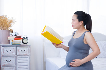 Pregnant woman reading a yellow book in the room.
