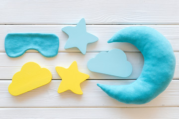 Sleep time concept with moon, stars, clouds, blindfolder on white wooden background top view