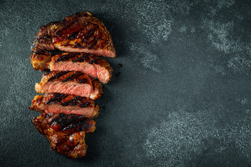 Sliced steak ribeye, grilled with pepper, garlic, salt and thyme on a dark stone background. Top view with copy space. Flat lay