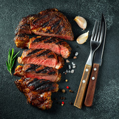 Sliced steak ribeye, grilled with pepper, garlic, salt and thyme on a dark stone background. Top view. Flat lay