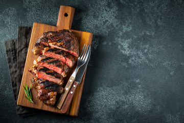 Fototapeta Sliced steak ribeye, grilled with pepper, garlic, salt and thyme served on a wooden cutting Board on a dark stone background. Top view with copy space. Flat lay obraz