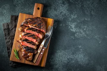 Poster Sliced steak ribeye, grilled with pepper, garlic, salt and thyme served on a wooden cutting Board on a dark stone background. Top view with copy space. Flat lay © Vasiliy