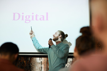 Waist up portrait of contemporary bearded man giving presentation pointing at word DIGITAL on...