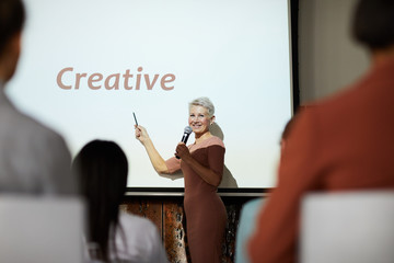 Portrait of successful businesswoman giving speech on creativity while standing on stage at...