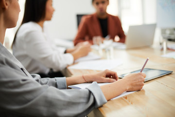 Closeup of unrecognizable businesswoman holding pen and paper listening to colleagues at meeting table, copy space