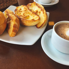Brazilian breakfast.  Capuccino cup and toasted bread with butter background.