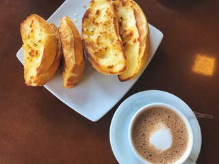 Brazilian breakfast.  Capuccino cup and toasted bread with butter background.