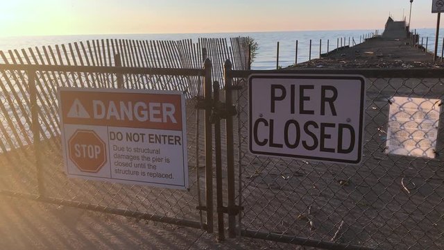 Pier closed signs of danger where a beach is not safe and falling into disrepair. Danger beach with a broken fishing pier.