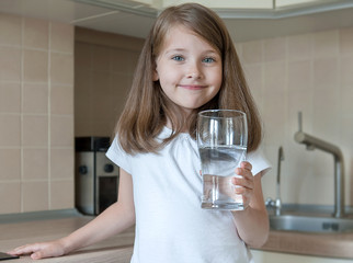 Portrait of a little caucasian baby girl holding a glass of tap clean water. Kitchen faucet. Cute...