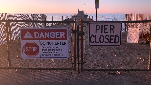 Pier closed signs of danger where a beach is not safe and falling into disrepair. Danger beach with a broken fishing pier.