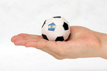 Mini football in hand and one black point of football is Argentina flag on white background.