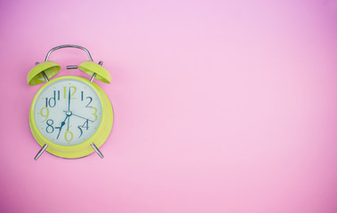 Bright green alarm clock lying on pink pastel background with copy space..