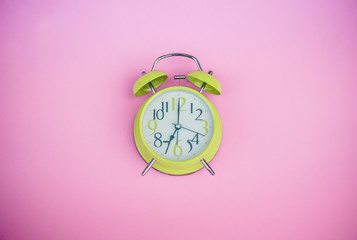 Bright green alarm clock lying on pink pastel background with copy space..